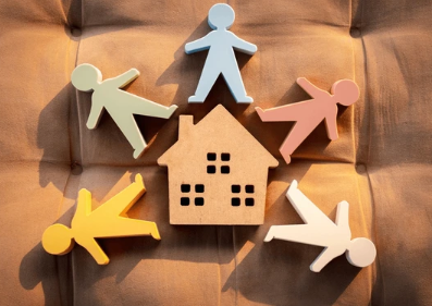 Paper figures gathered around a wooden house, representing support and belonging